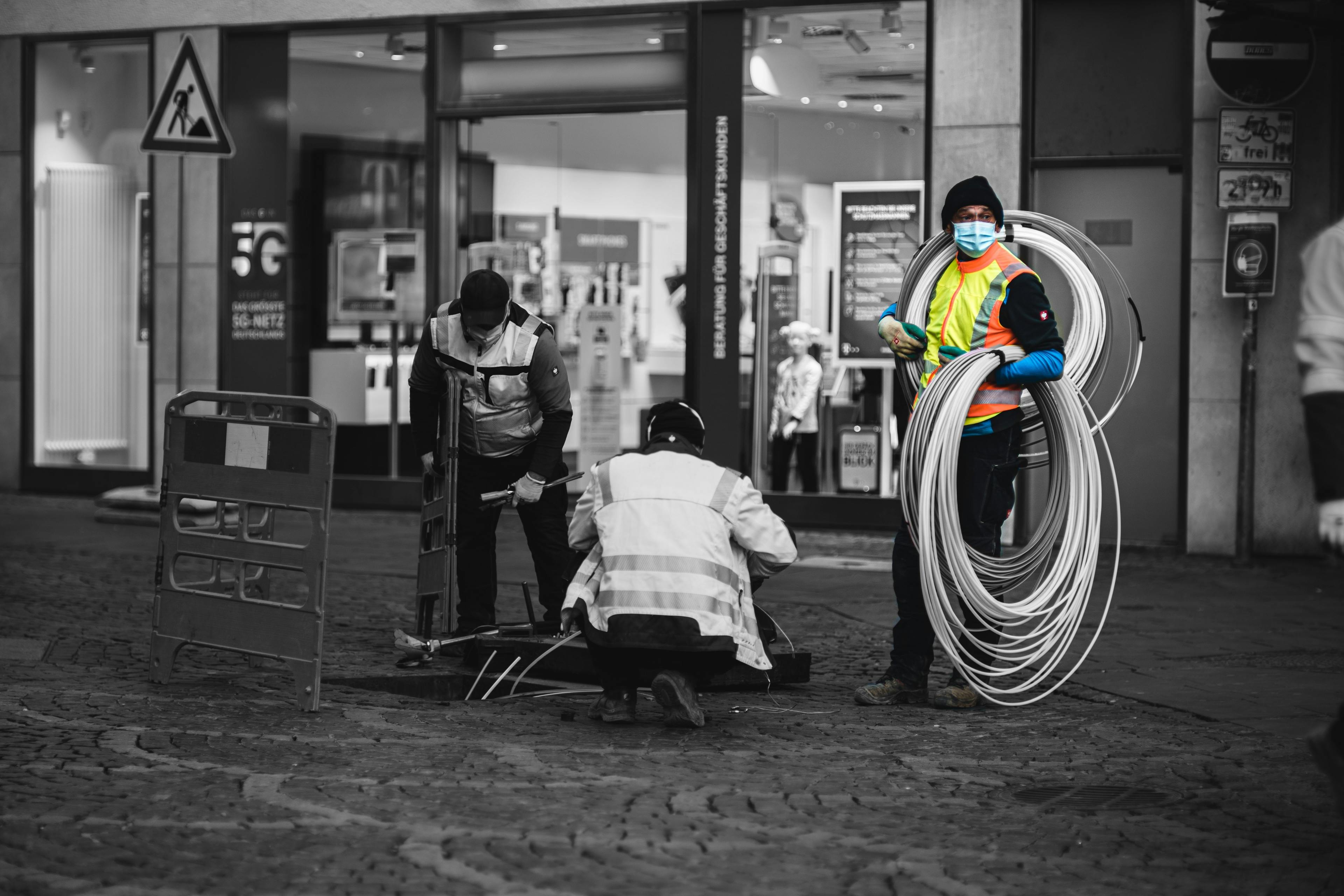 Three workers in high vis jackets installing broad band cable into the ground on a UK high street