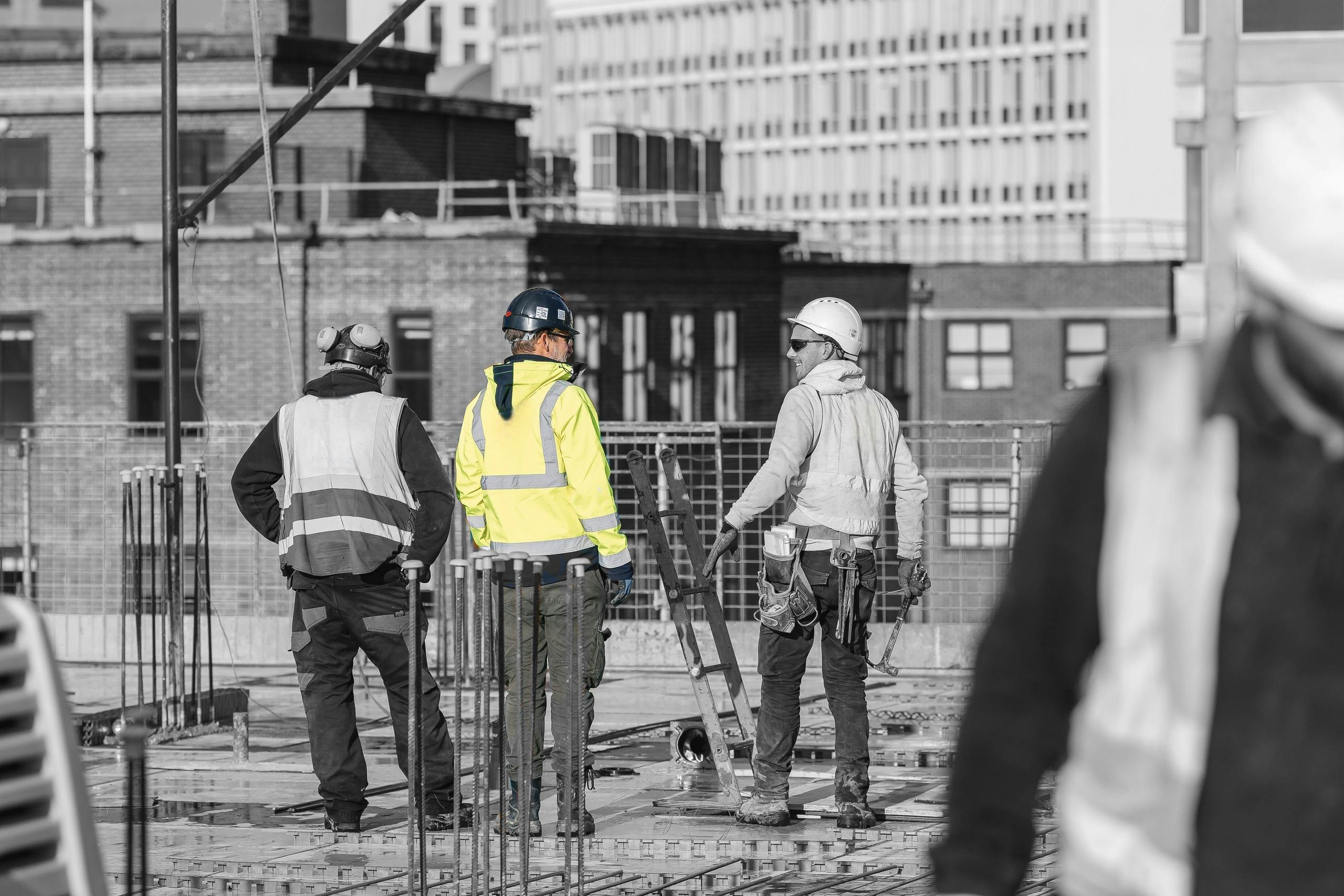 Three workmen in protective clothing on the roof of a construction site talking on a sunny day