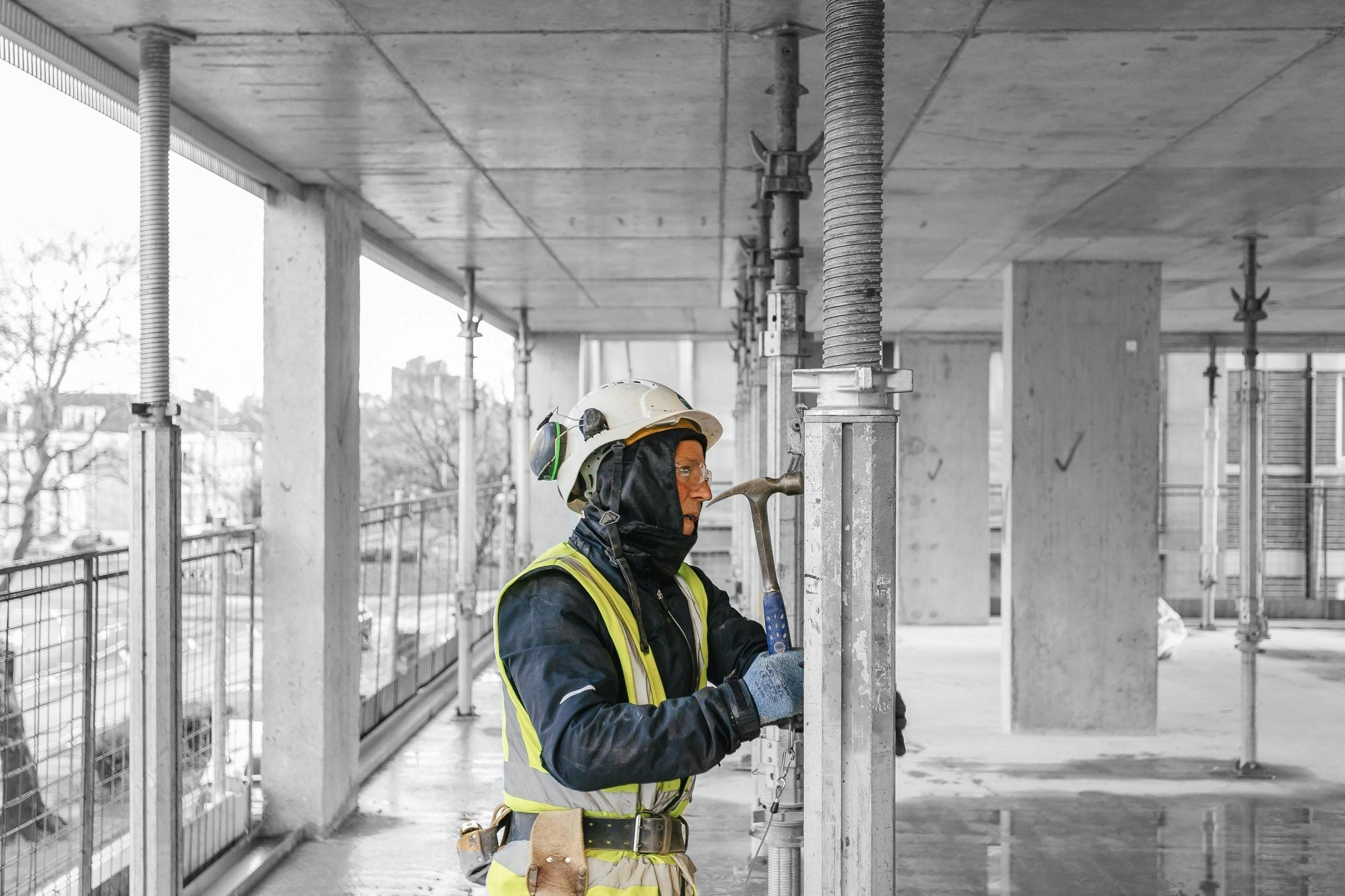 Man working on construction site wearing protective clothing using a hammer on scaffolding