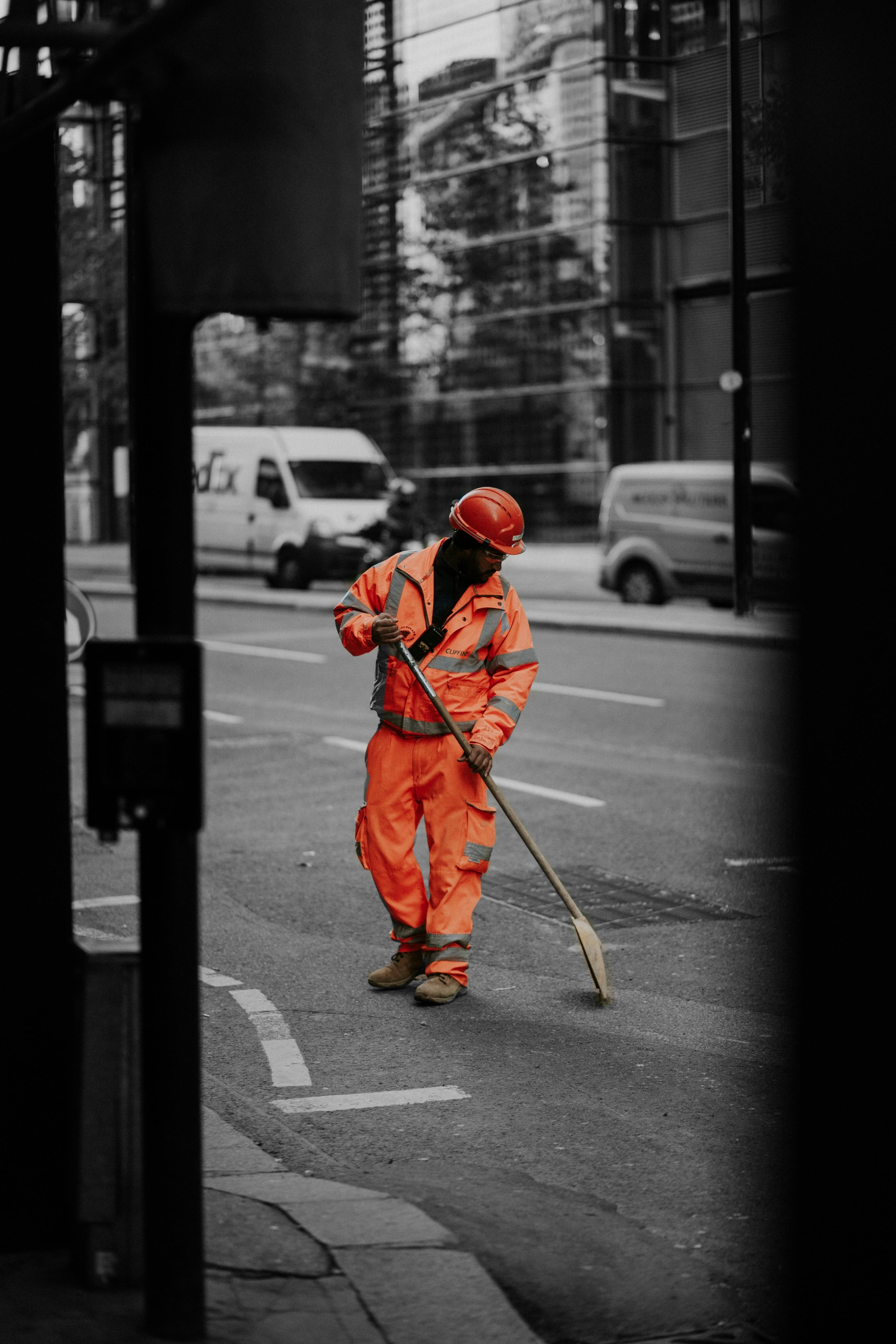 Construction worker wearing orange protective clothing and hard hat removing material from road using a shovel