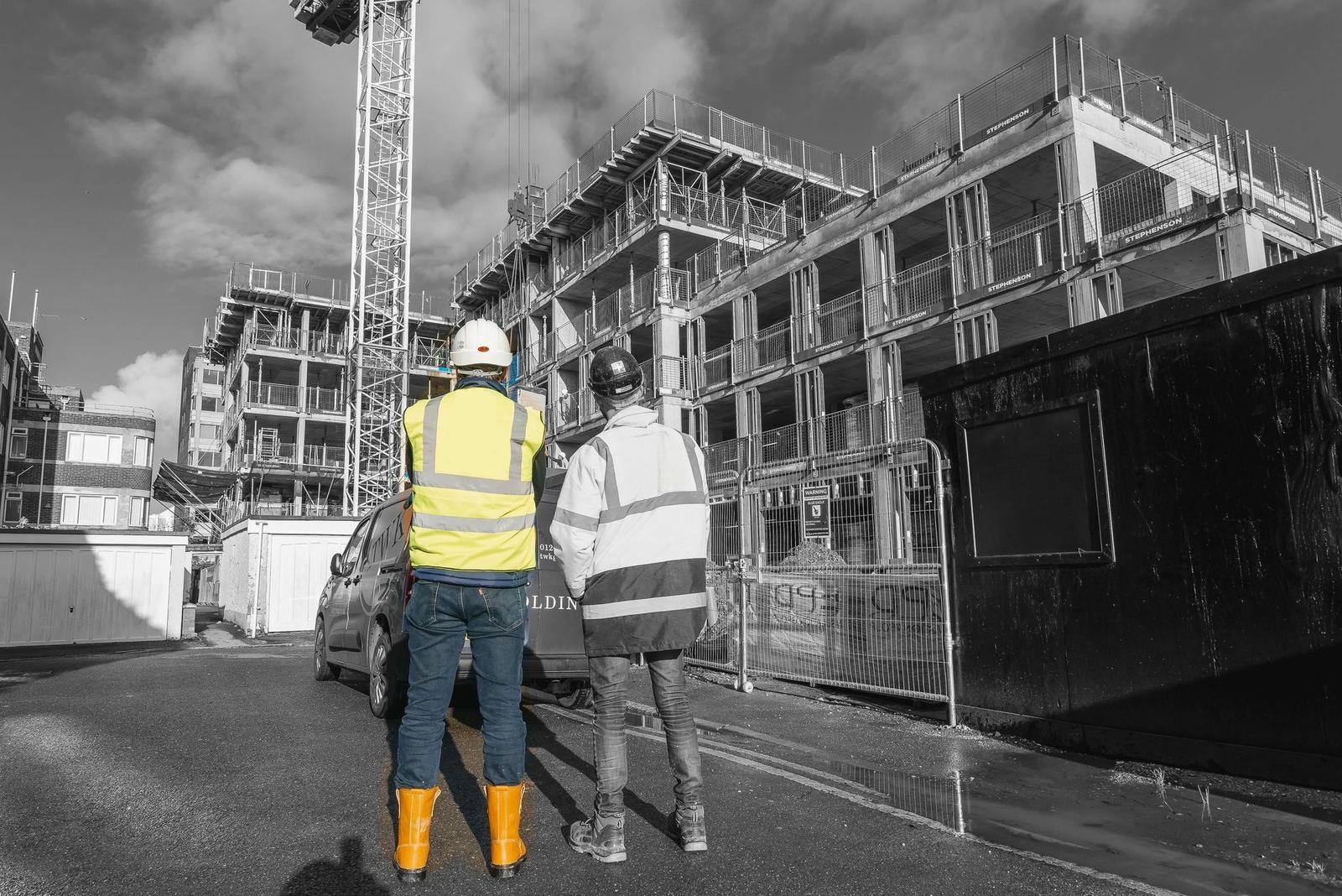 Two construction workers in hard hats looking at a building site 
