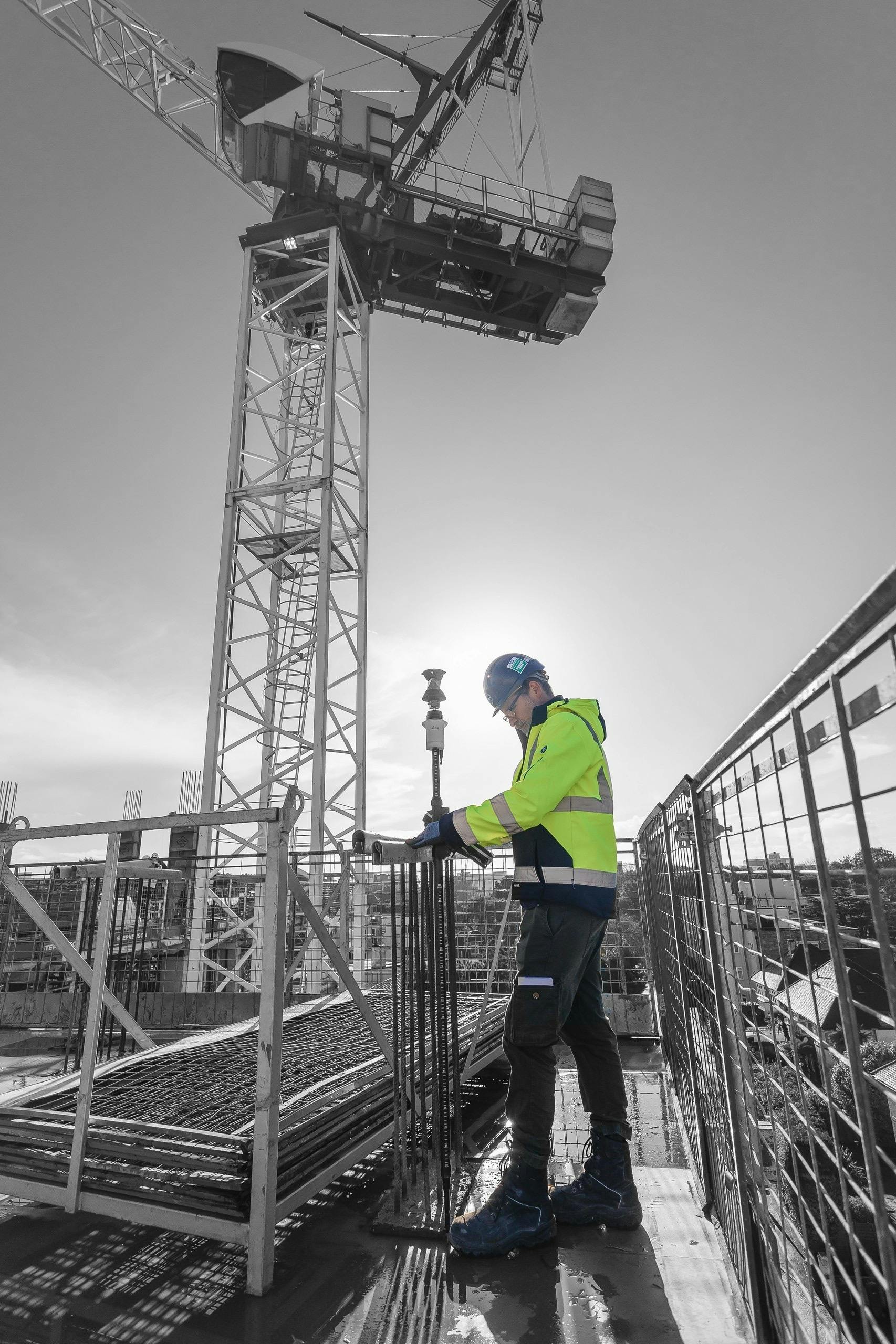 Surveyor on a building site in protective clothing taking measurements with the crane and sun in the background
