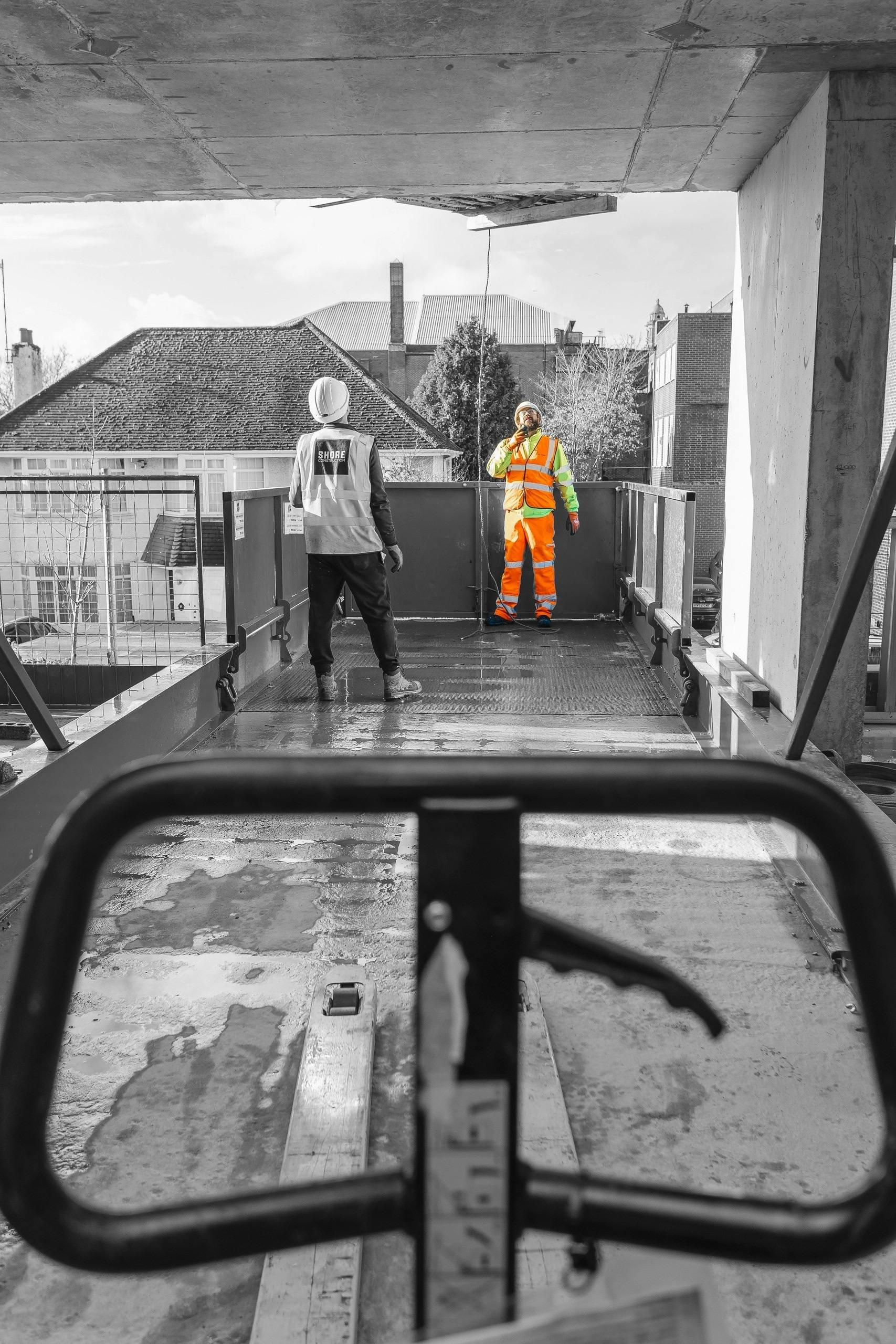 Two construction workers in protective clothing looking upwards and guiding a crane lowering equipment on to a building site 