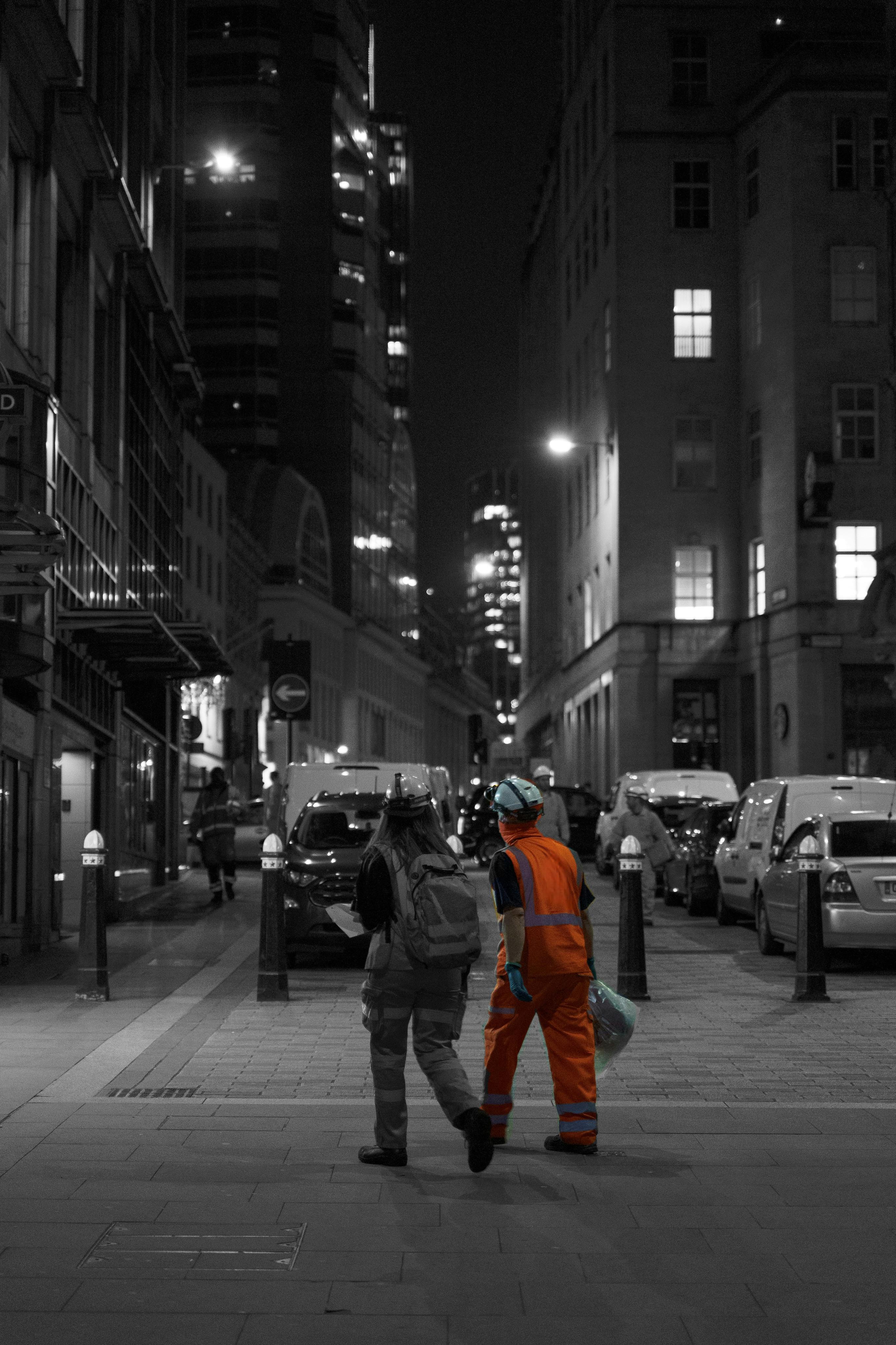 Two construction workers in protective clothing walking across a road at night in central London