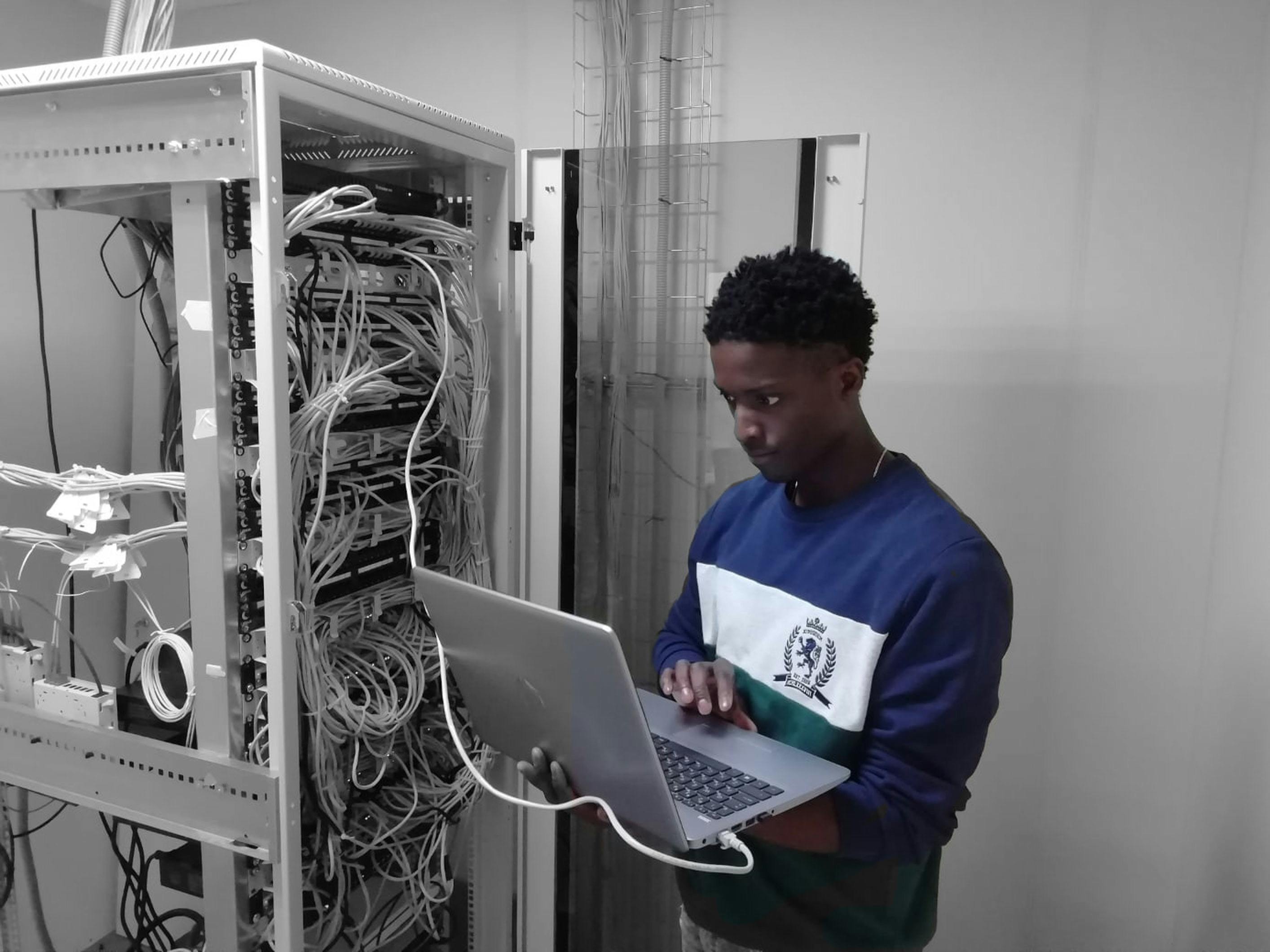 IT technician reads from a laptop connected to a server by a data cable