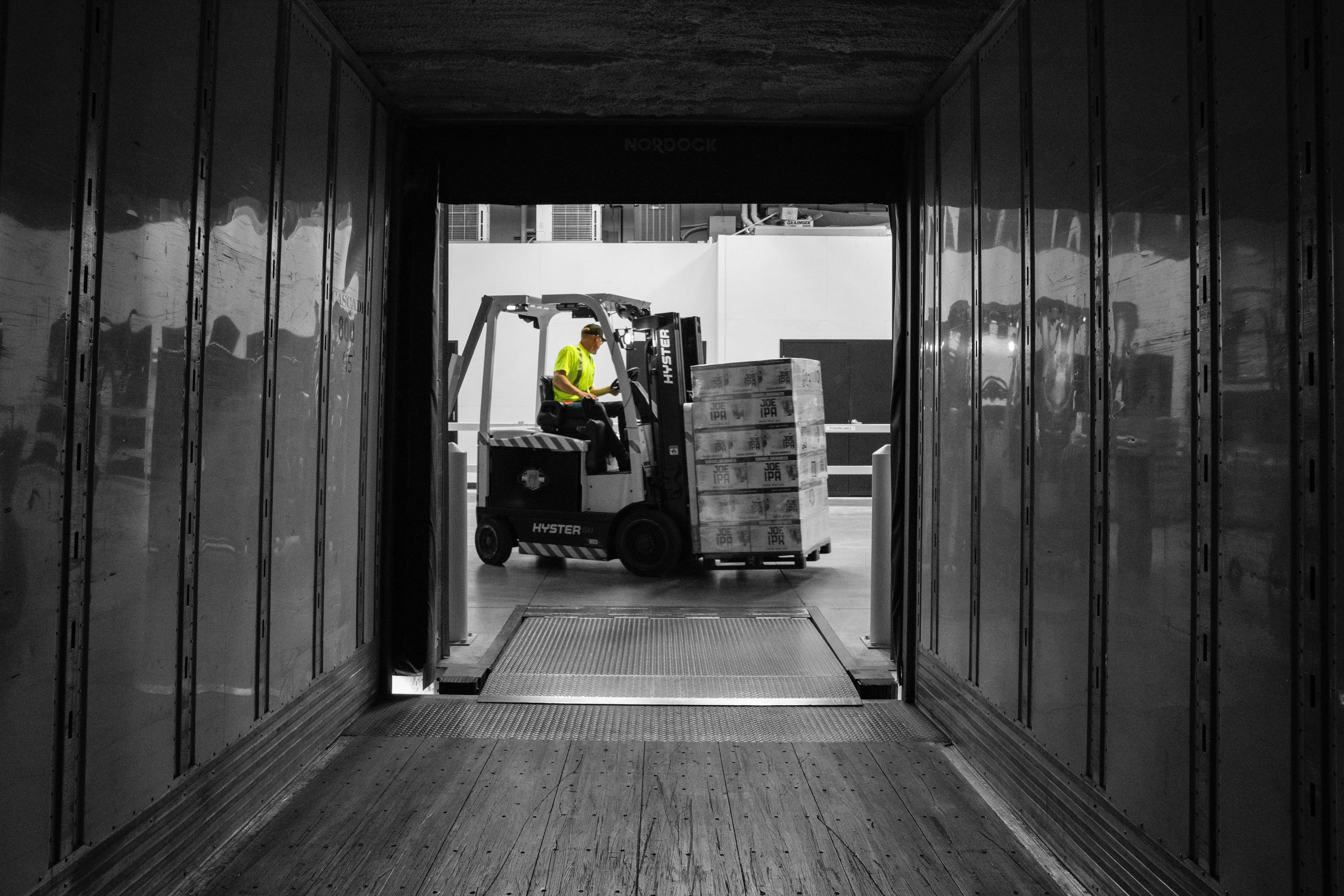 Picture from inside lorry trailer as male forklift truck driver removes a pallet