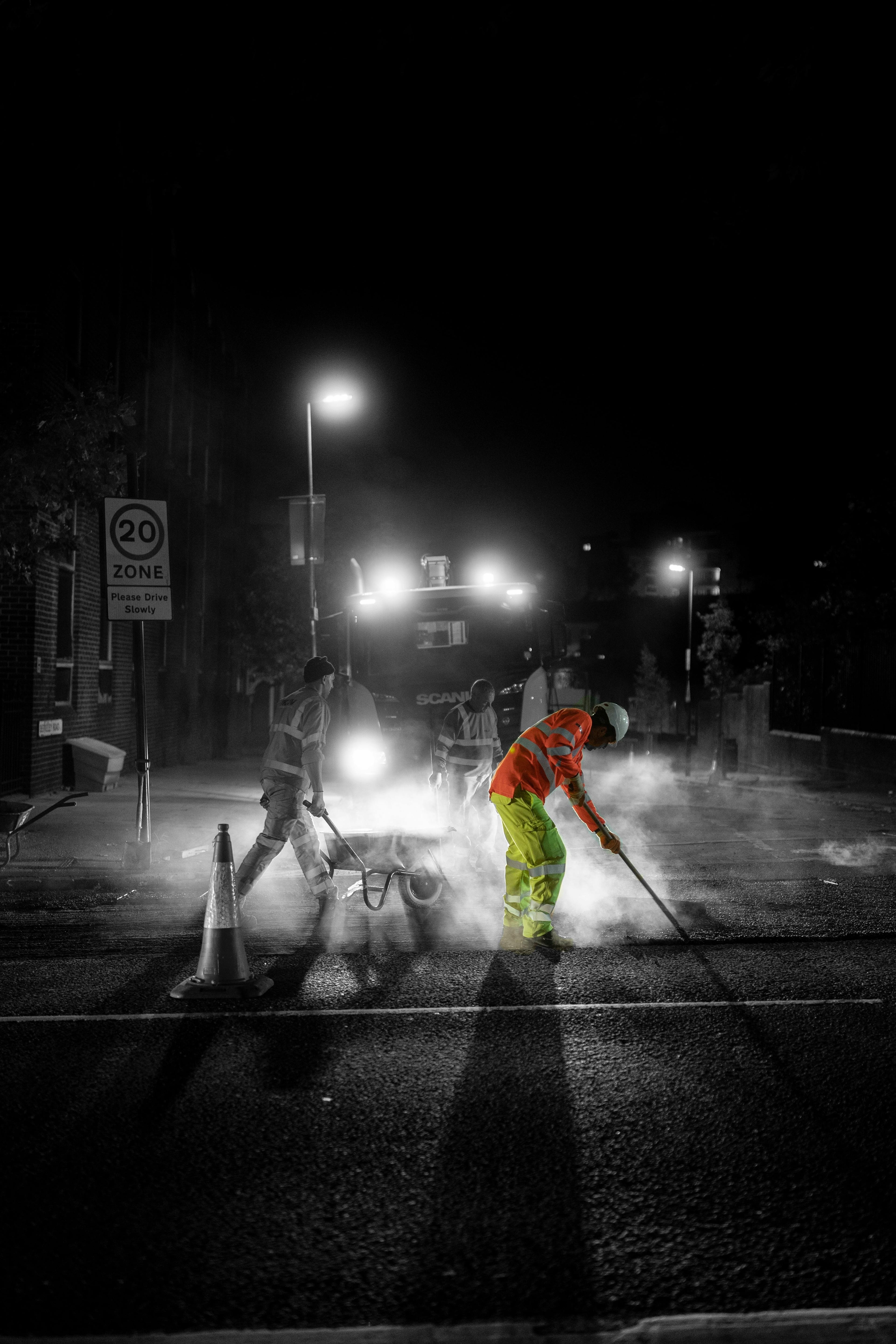 Three highway repair workers working at night on UK road fixing a hole
