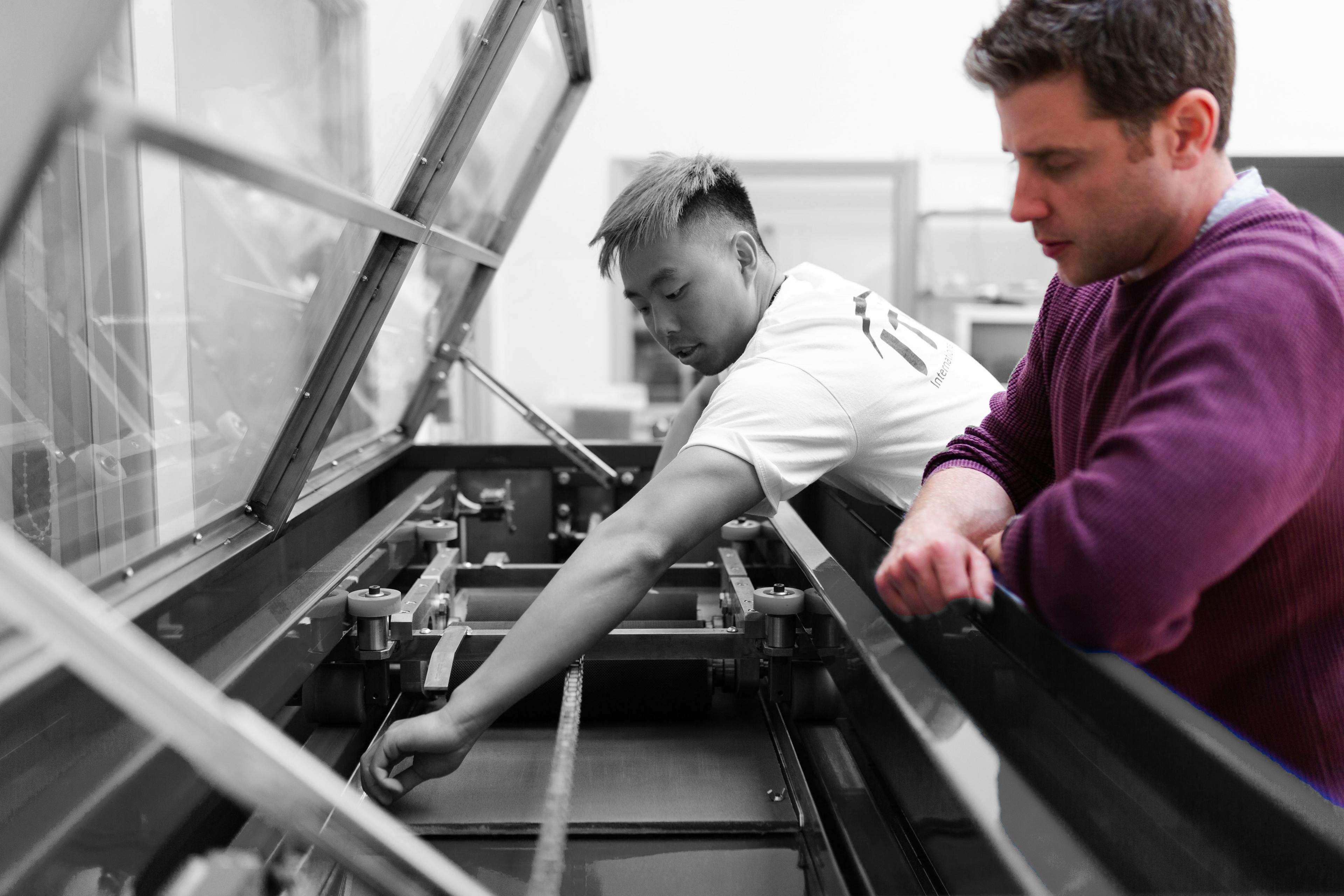A worker or student inspects a large format printer with a manager or colleague next to him
