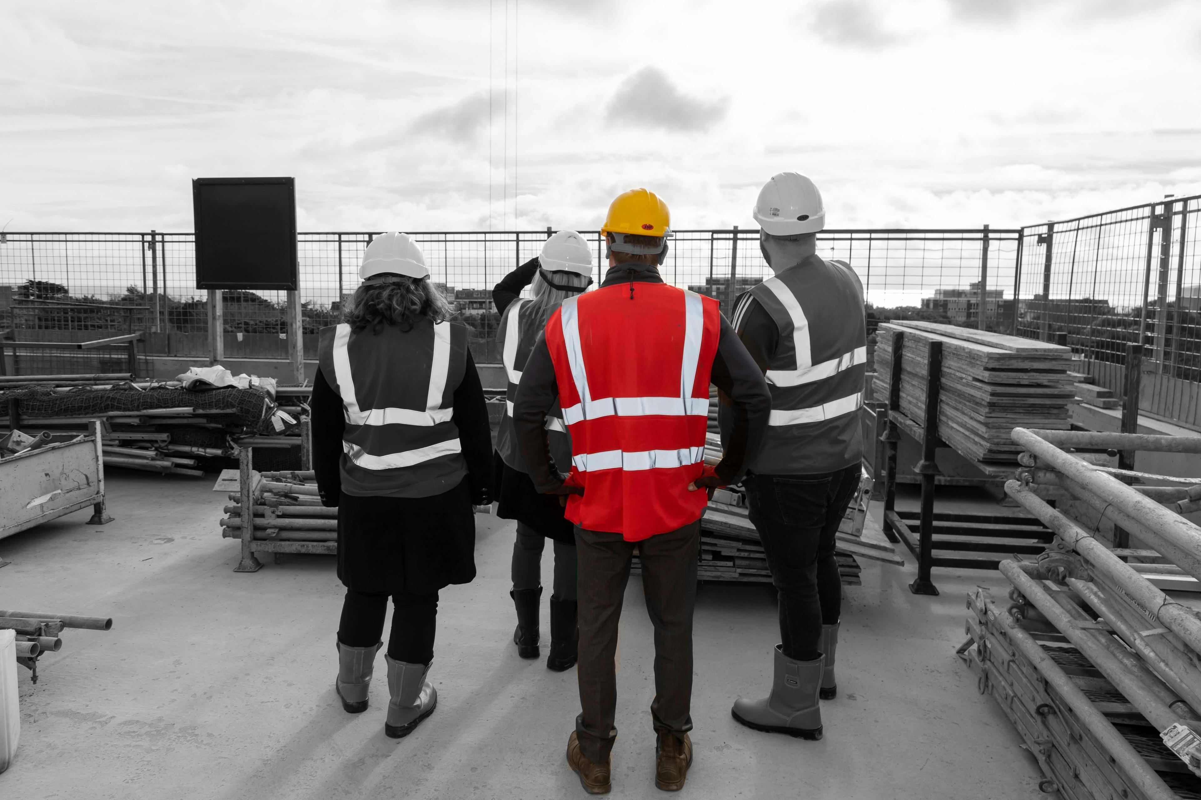 Four construction managers in hi vis jackets inspecting a building project standing on the roof of a new building surrounded by building materials