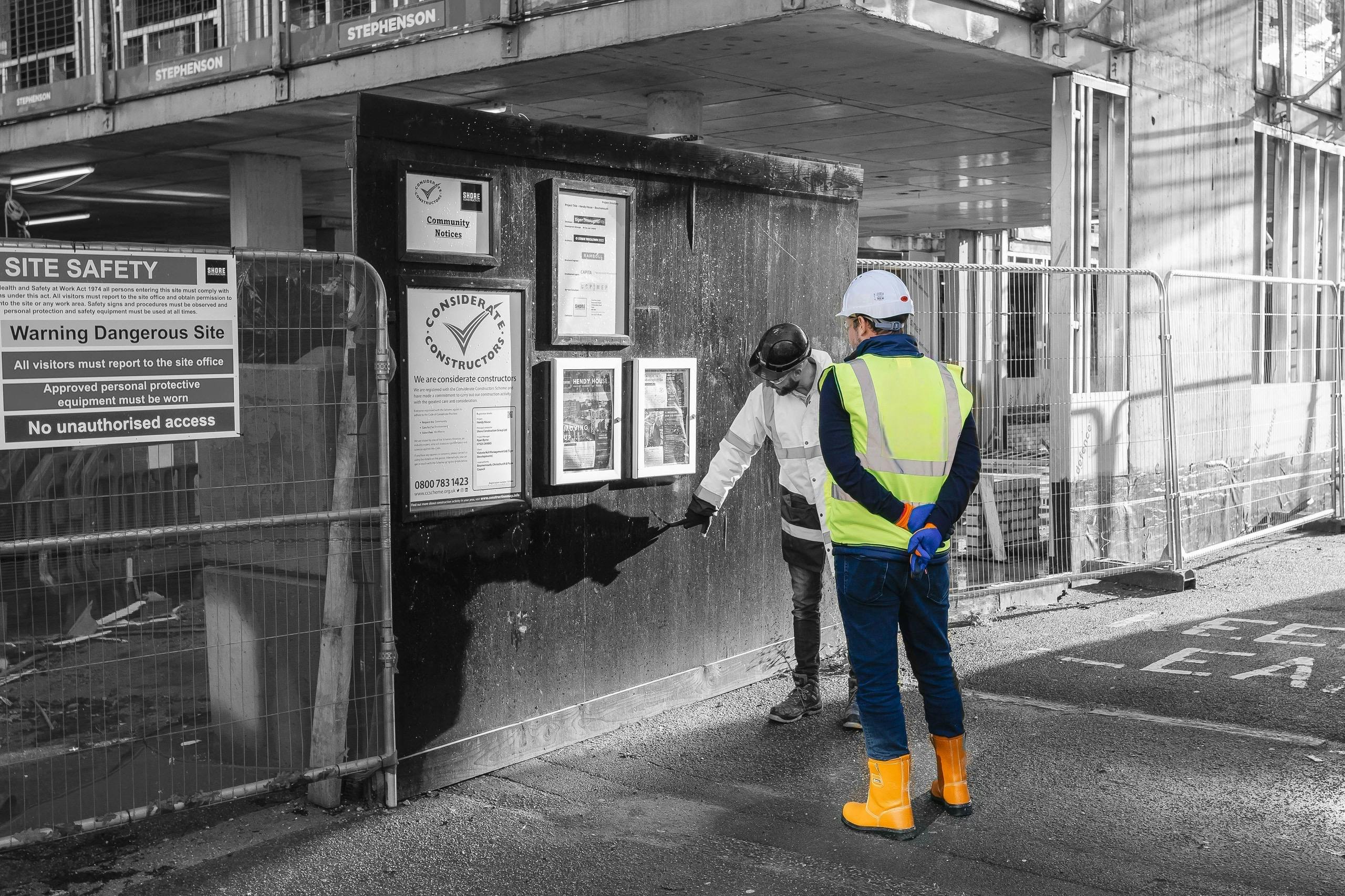 Two construction workers inspecting notice boards outside a building site