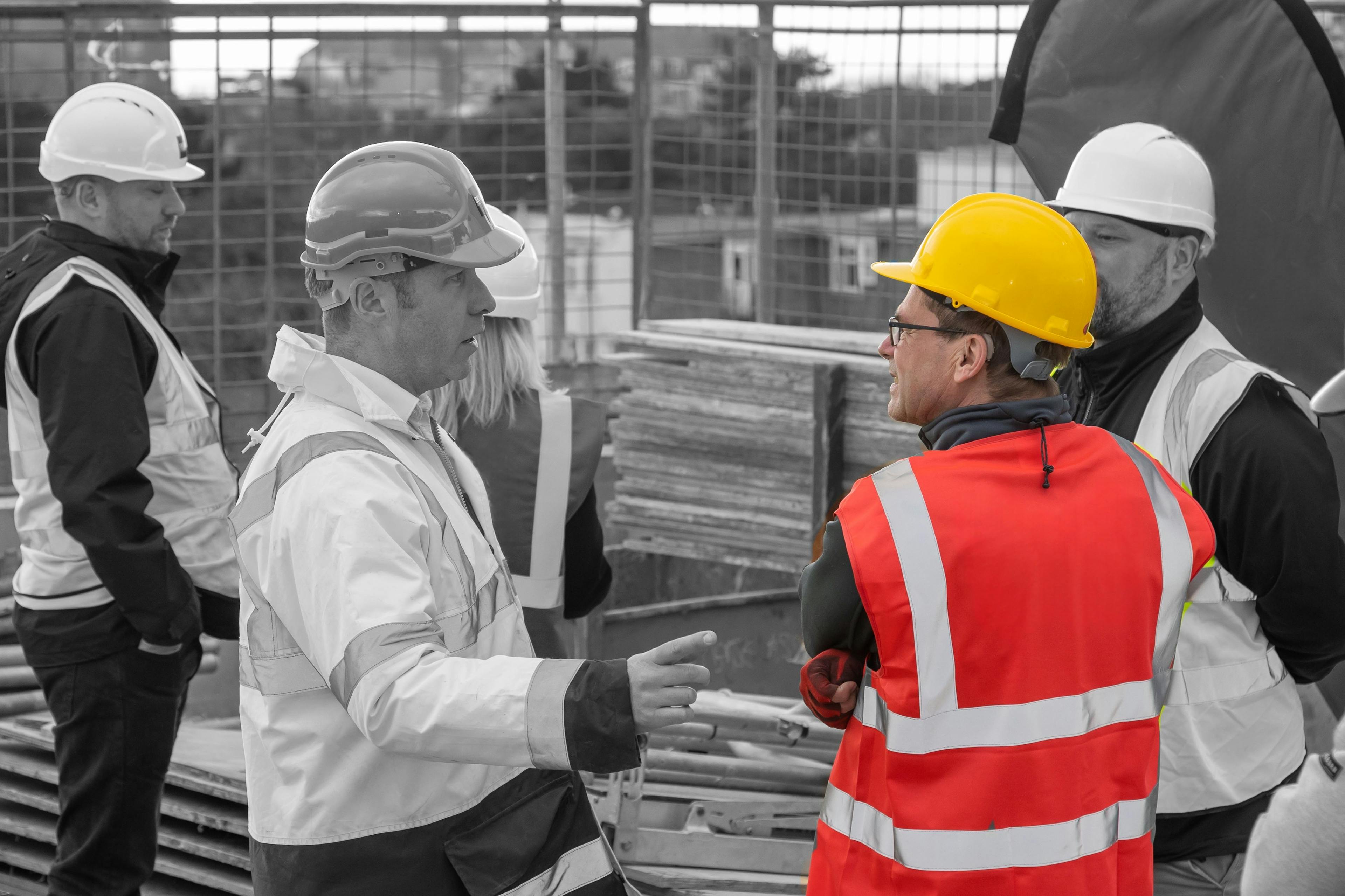 A group of people, all wearing high-vis jackets, having separate conversations on a construction site
